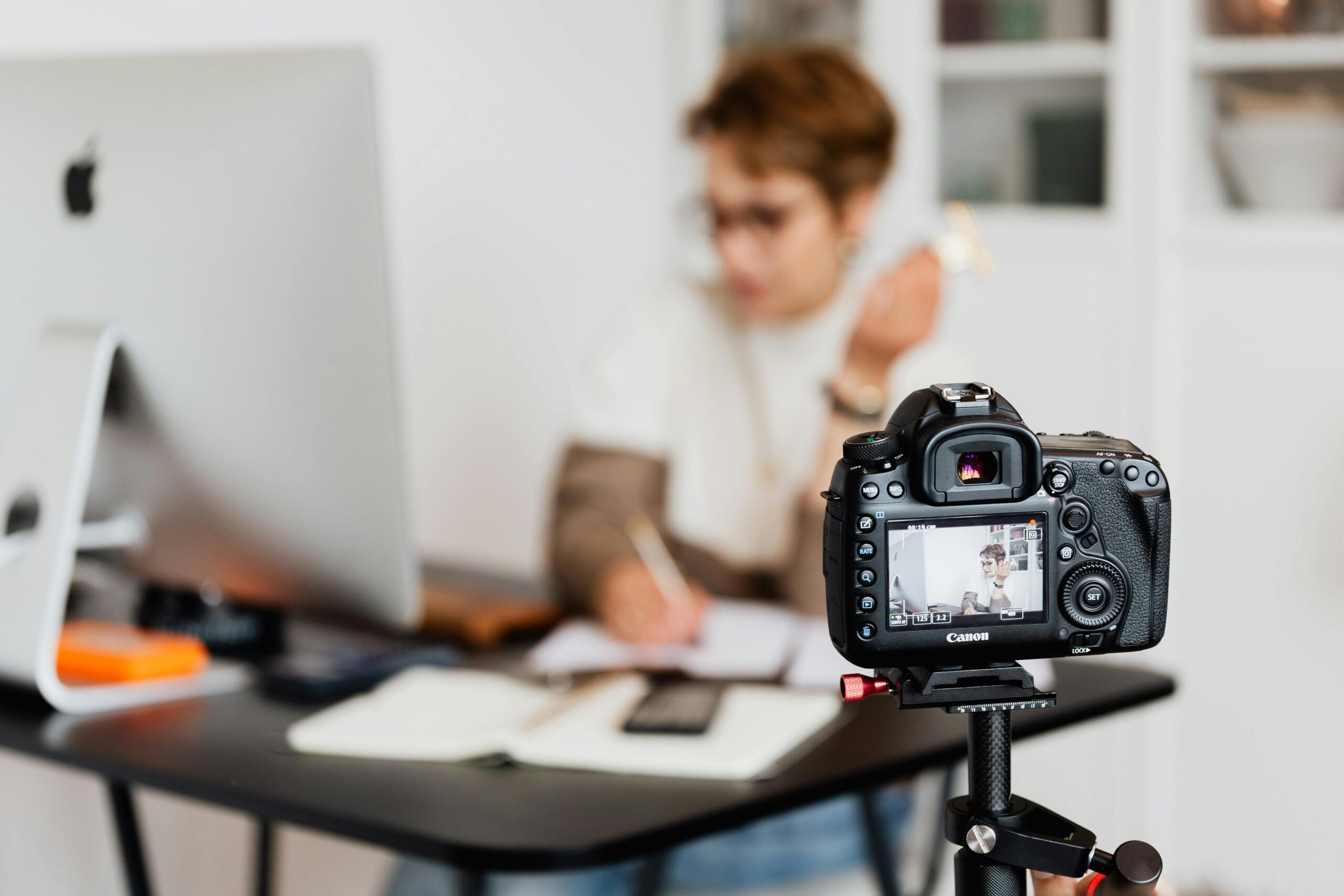 Home Unrecognizable blurred lady working at table in modern office against photo camera placed on tripod