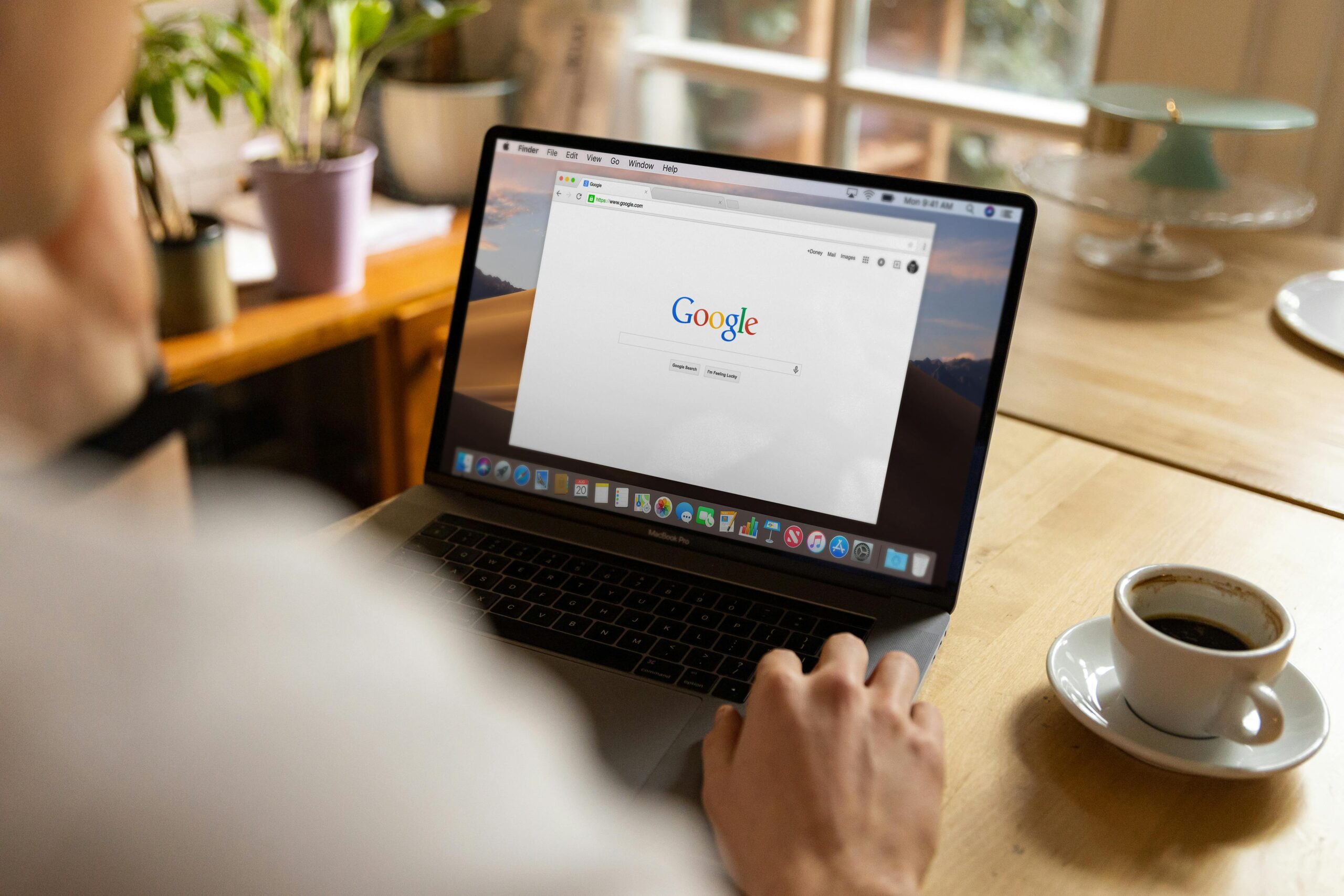 Home An adult using a laptop indoors, browsing Google at a wooden table with coffee.